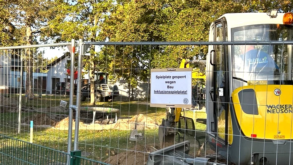 Ein abgesperrter Spielplatz mit Bauzaun, Bagger und Erdarbeiten zeigt den Beginn der Bauarbeiten für den neuen Inklusionsspielplatz.