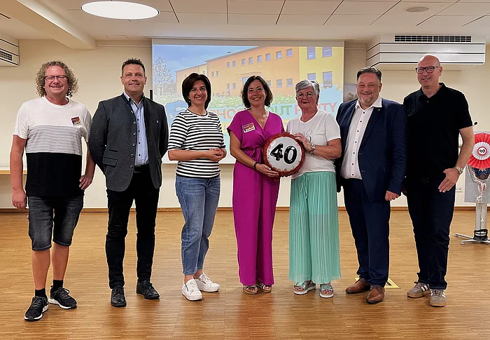 Sieben Personen stehen bei einer Feierstunde im Mehrgenerationenhaus nebeneinander, in der Mitte wird ein symbolisches Jubiläumszeichen mit der Zahl 40 präsentiert.