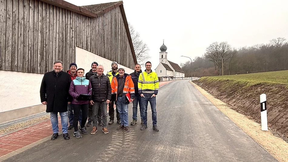 Eine Gruppe aus Vertreterinnen und Vertretern der Stadt, der Baufirma und der Planung steht gemeinsam auf der frisch fertiggestellten Straße „Am Seeberg“ in Dirnau, im Hintergrund die Kirche St. Martin.