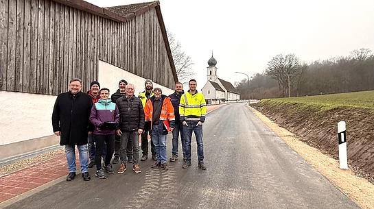Eine Gruppe aus Vertreterinnen und Vertretern der Stadt, der Baufirma und der Planung steht gemeinsam auf der frisch fertiggestellten Straße „Am Seeberg“ in Dirnau, im Hintergrund die Kirche St. Martin.