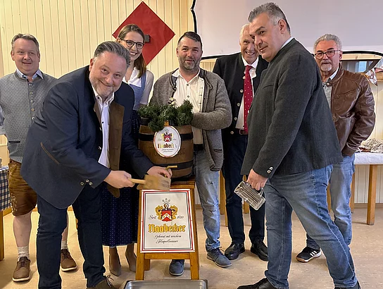Beim offiziellen Anzapfen schlägt der Bürgermeister den Zapfhahn in das Bierfass, während die Umstehenden zuschauen.