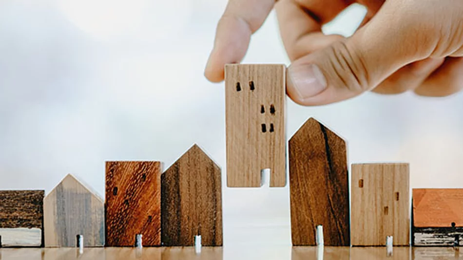 Das Foto zeigt eine Hand, die ein kleines Holzhaus zwischen weitere Holzhausmodelle stellt und damit sinnbildlich die Teilnahme von Haushalten am Mikrozensus darstellt.