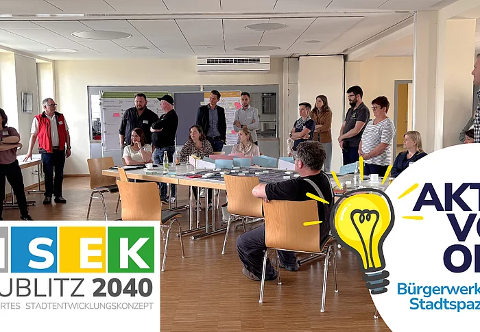 Mehrere Menschen sitzen und stehen um Tische in einem Seminarraum, während eine Person vorne spricht. Im Bild sind Logos und Schriftzüge zum Stadtentwicklungsprojekt „ISEK Teublitz 2040“ und „Aktiv vor Ort“ zu sehen.