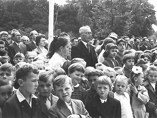 Schwarz-Weiß-Aufnahme der Einweihungsfeier des Teublitzer Schulhaus-Erweiterungsbaus im Jahr 1957. Zahlreiche Schulkinder stehen dicht gedrängt vor den erwachsenen Gästen und verfolgen die Feier.