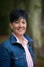 Eine Frau mit kurzem dunklem Haar und Jeansjacke lächelt offen.
