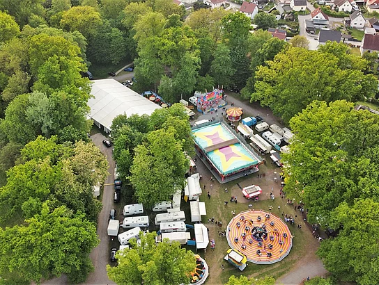 Aufnahme aus der Luft vom Festplatz im Stadtpark mit Festzelt und Fahrgeschäften.