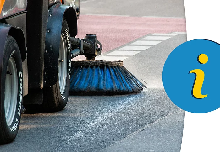 Eine Straßenkehrmaschine reinigt mit rotierender Bürste die Fahrbahn am Straßenrand, während ein Hinweis-Symbol auf wichtige Informationen aufmerksam macht.
