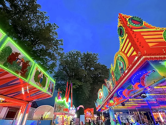 Eine zulaufende Gasse am Volksfestplatz mit bunt leuchtenden Verkaufsfenstern.