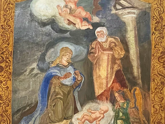 Nahaufnahme eines restaurierten Deckengemäldes in der Marien-Wallfahrtskirche Saltendorf. Das von einem reich verzierten, goldbraunen Rahmen eingefasste Gemälde zeigt Maria und Josef mit dem Jesuskind sowie Engel. Die Farben und Konturen der Figuren sind deutlich erkennbar.