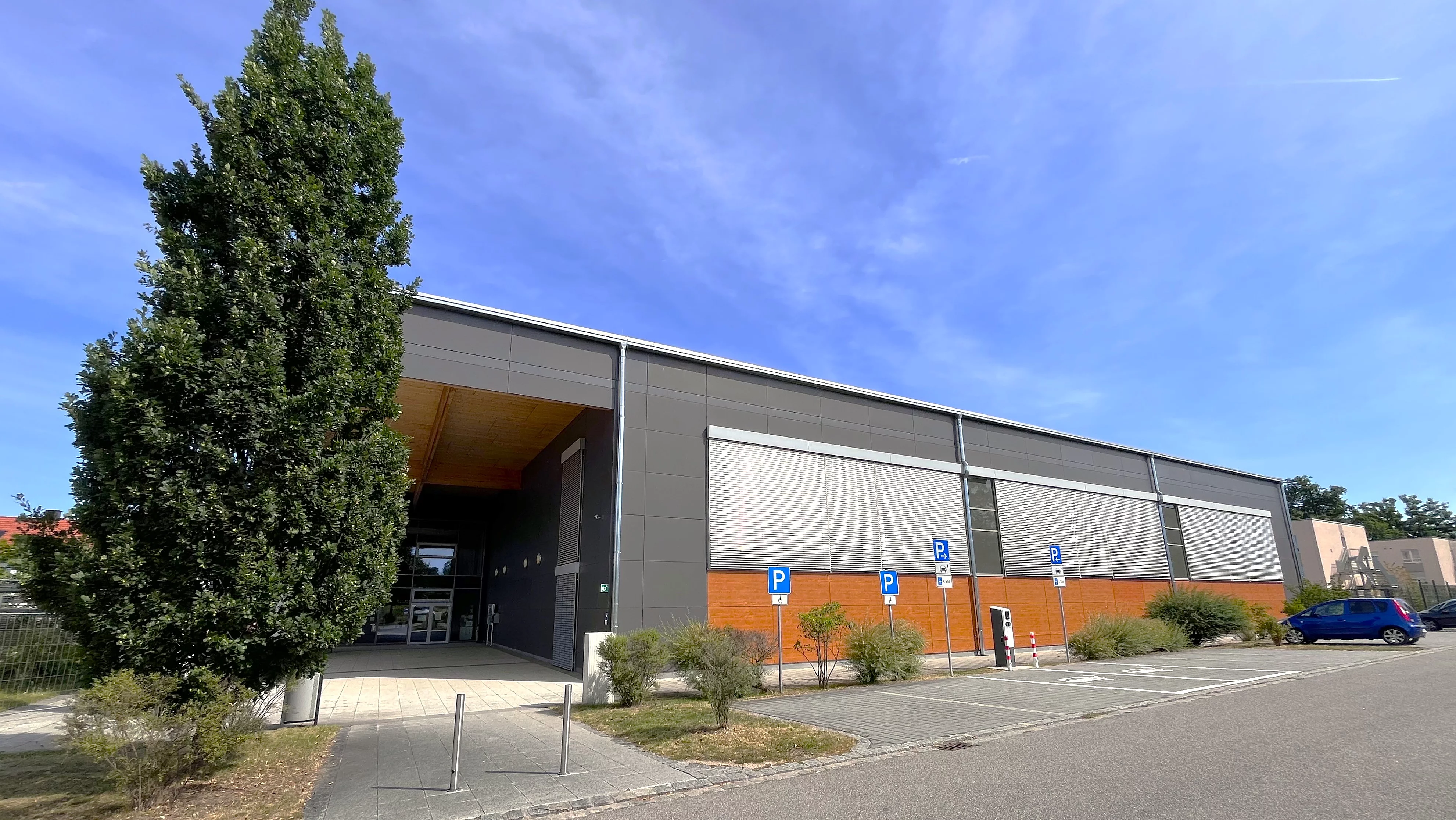 Grünanlagen im Vordergrund, dahinter der Eingangsbereich der Dreifachsporthalle.
