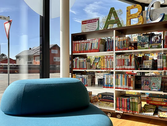 Bücherregal mit Kinderbüchern steht neben einem Fenster mit Blick auf die Straße.