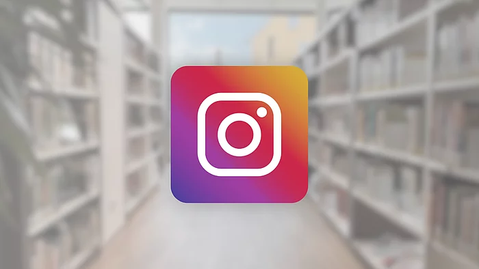 Das Instagram-Logo ist vor einem unscharfen Hintergrund mit Bücherregalen abgebildet.