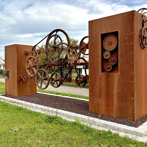 Eine verrostete Skulptur mit alten Zahnrädern und Stehlen.