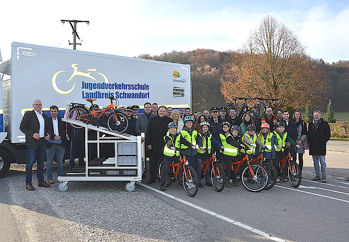 Kinder mit Fahrrädern, Lehrkräfte, Polizei und Vertreterinnen und Vertreter des Landkreises posieren vor dem neuen Lkw der Jugendverkehrsschule für ein gemeinsames Foto.