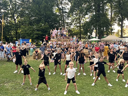 Kinder tanzen im Kinderland vor der Pyramide aus Stroh.