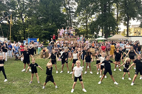 Kinder tanzen im Kinderland vor der Pyramide aus Stroh.