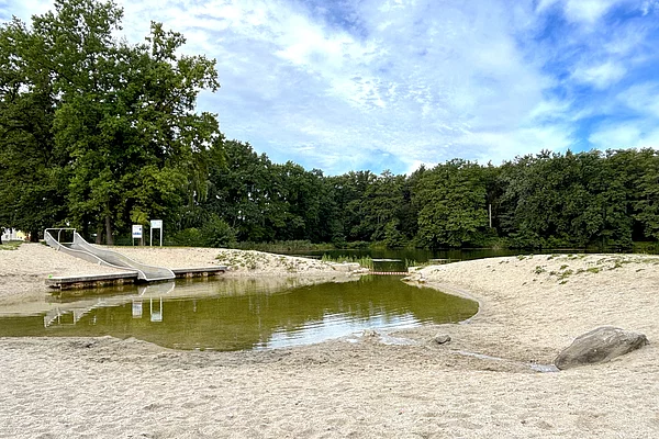Ein kleines Becken an dessen linkem Ufer eine große Wellen-Wasserrutsche mündet.