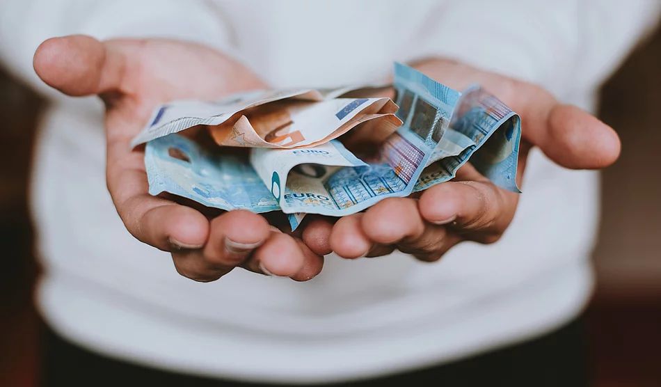 Aufgeschlagene Hände eines Mannes auf dem Bargeld liegt, das symbolisch gereicht werden.