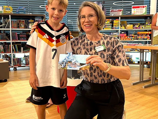 Der Gewinner des Hauptpreises steht gemeinsam mit Büchereileiterin Corinna Höfler in der Stadtbücherei und präsentiert seinen gewonnenen Gutschein.