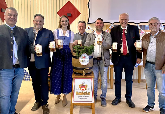 Mehrere Vertreter und Organisatoren stehen gemeinsam um ein Bierfass der Brauerei Naabecker und halten gefüllte Bierkrüge in die Kamera.
