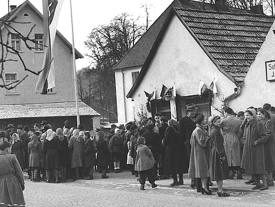 Eine historische Schwarz-Weiß-Aufnahme zeigt zahlreiche Menschen, die sich vor dem damaligen Jugendheim in Teublitz versammelt haben. Vor dem Gebäude weht eine große Fahne an einem Mast. Erwachsene und Kinder stehen dicht gedrängt entlang der Straße und warten auf die Eröffnung des neuen Treffpunkts.