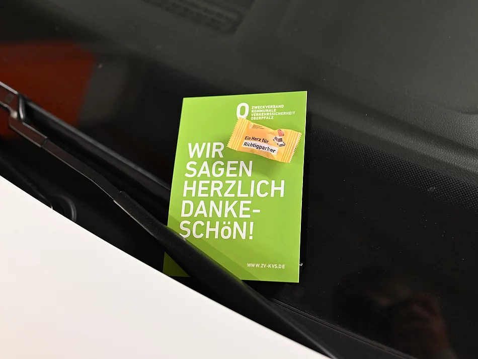 Eine grüne Dankeskarte des Zweckverbands Kommunale Verkehrssicherheit Oberpfalz steckt hinter dem Scheibenwischer eines Autos und trägt den Schriftzug ‚Wir sagen herzlich Dankeschön!‘ sowie den Hinweis auf eine kleine Aufmerksamkeit für korrekt parkende Verkehrsteilnehmer.