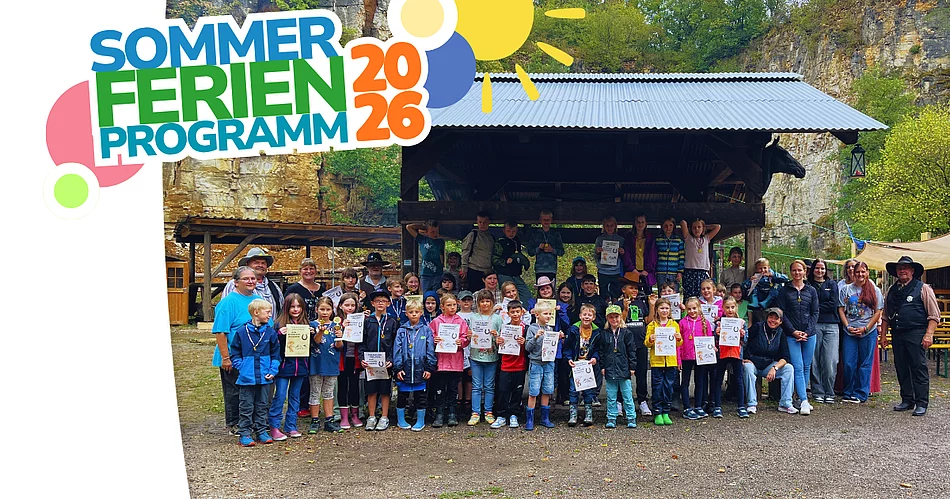 Eine große Gruppe von Kindern und Erwachsenen steht bei einem Kinder-Rodeo im Freien vor einer überdachten Holzhütte; viele Kinder halten Urkunden in den Händen.