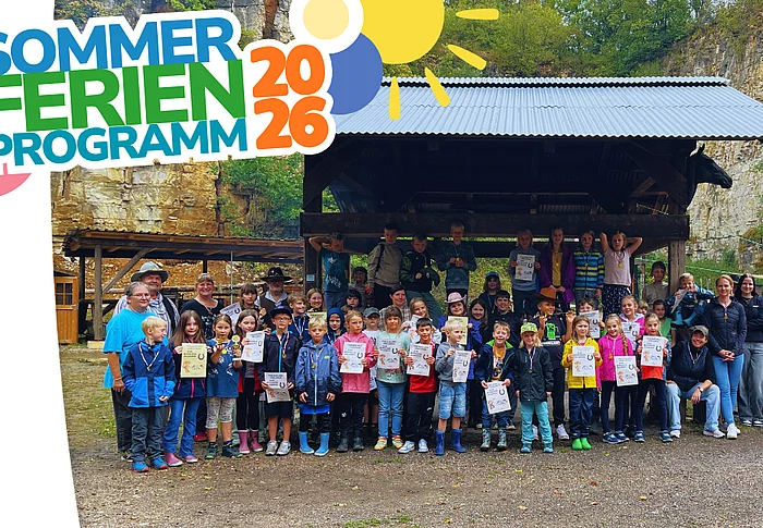 Eine große Gruppe von Kindern und Erwachsenen steht bei einem Kinder-Rodeo im Freien vor einer überdachten Holzhütte; viele Kinder halten Urkunden in den Händen.