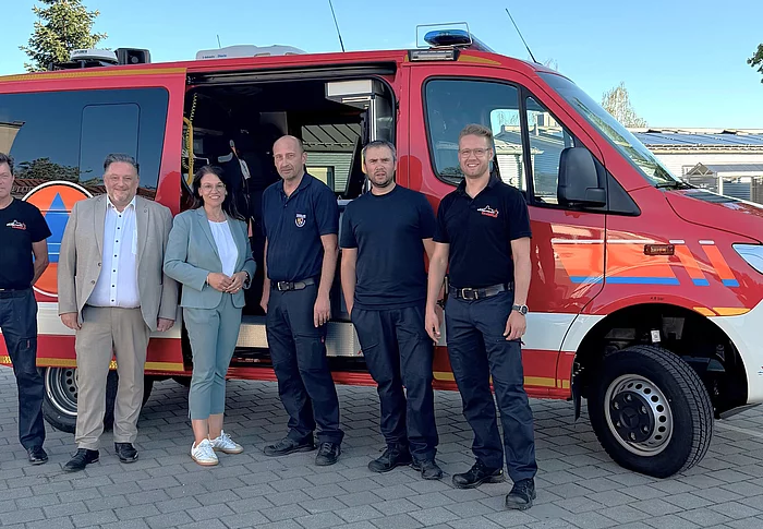Sechs Personen stehen vor dem neuen roten CBRN-Erkundungswagen der Freiwilligen Feuerwehr Teublitz. Zu sehen sind Vertreter der Feuerwehr sowie Erster Bürgermeister Thomas Beer, die Parlamentarische Staatssekretärin Martina Englhardt-Kopf und Kreisbrandrat Christian Demleitner. Das Einsatzfahrzeug ist seitlich mit geöffneter Schiebetür abgebildet.