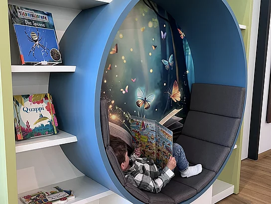 Ein Kind liest entspannt in einer runden, gemütlichen Lesehöhle im Regal.