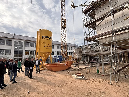 Eine Baustelle mit Gerüst, Baukran und einem großen gelben Baustoffsilo zeigt ein Gebäude im Rohbauzustand.