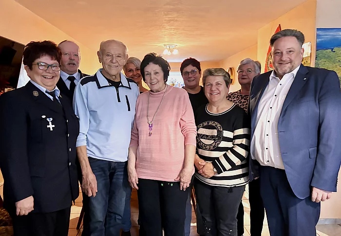 Eine fröhliche Gruppe von Menschen steht in einem Wohnzimmer eng beisammen und lächelt in die Kamera, offenbar anlässlich eines besonderen Geburtstags.