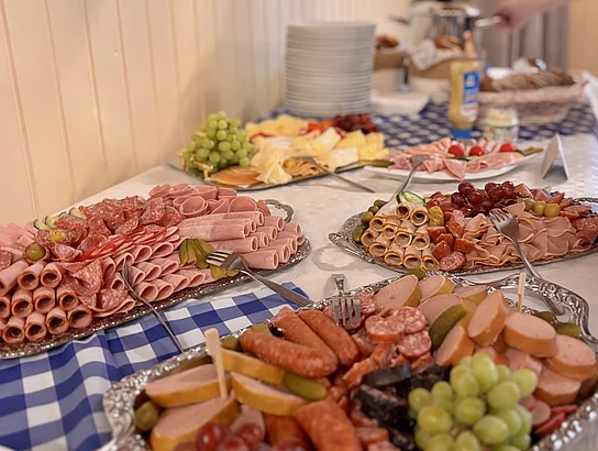 Auf einem Buffet sind verschiedene Brotzeitplatten mit Wurst, Aufschnitt, Käse, Trauben und Garnituren für die Gäste vorbereitet.