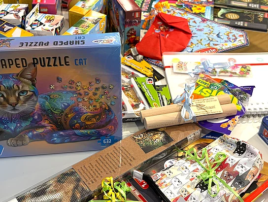 Auf einem Tisch liegen zahlreiche Preise für den Sommerferien-Leseclub, darunter Spiele, Puzzles, Bücher, Bastelmaterialien und weitere Geschenke.