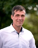 Ein Mann mit kurzem dunklem Haar und Hemd blickt entspannt in die Kamera.