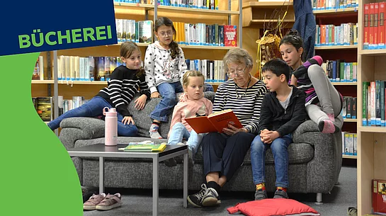 Ein Werbebild für die Stadtbücherei zeigt eine ältere Frau, die mehreren Kindern auf einem Sofa aus einem Buch vorliest. Die Kinder sitzen aufmerksam um sie herum und hören gespannt zu. Im Hintergrund sind Bücherregale der Bücherei zu sehen. Links oben steht gut sichtbar der Schriftzug „BÜCHEREI“.