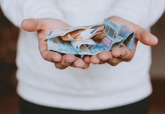 Aufgeschlagene Hände eines Mannes auf dem Bargeld liegt, das symbolisch gereicht werden.