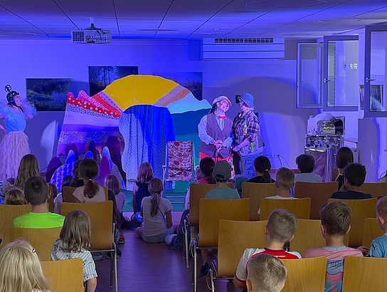 Die Schauspielerinnen und Schauspieler stehen auf der Bühne, während zahlreiche Kinder aufmerksam im Publikum sitzen.
