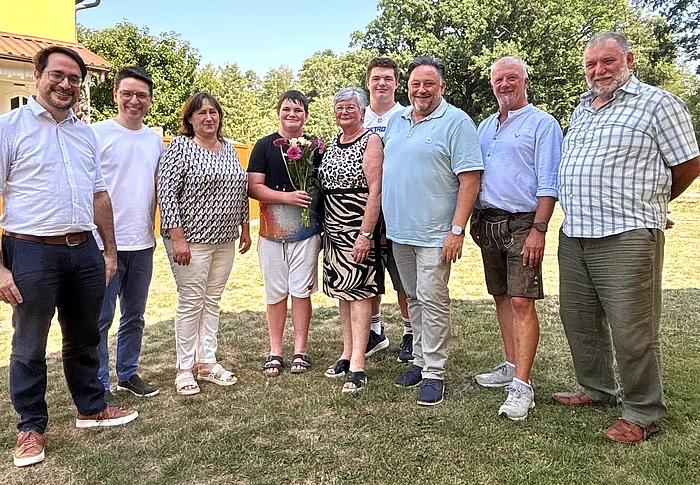 Bürgermeister Thomas Beer steht gemeinsam mit der Jubilarin Romy Hermann-Reisinger sowie mehreren Familienangehörigen und Wegbegleitern im Garten für ein Erinnerungsfoto anlässlich ihres 70. Geburtstags.