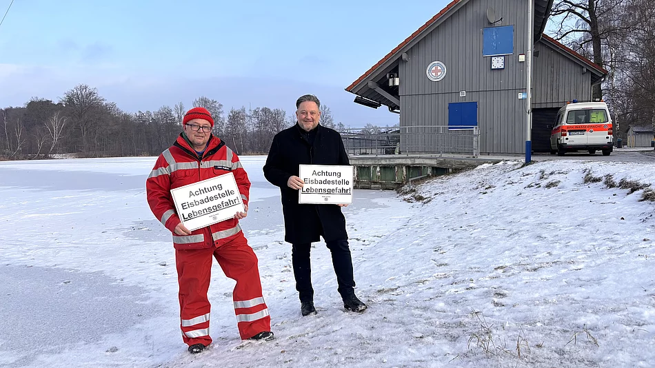 Ein Vertreter der Wasserwacht und der Erste Bürgermeister warnen an einem zugefrorenen Gewässer eindringlich vor den lebensgefährlichen Risiken von Eisflächen.