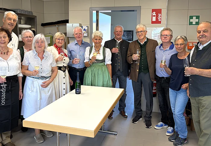 Die Mitglieder des Seniorenbeirats stehen vor Beginn des Oktoberfests gemeinsam in der Küche des Mehrgenerationenhauses und halten zum Teil Gläser zum Anstoßen in den Händen.