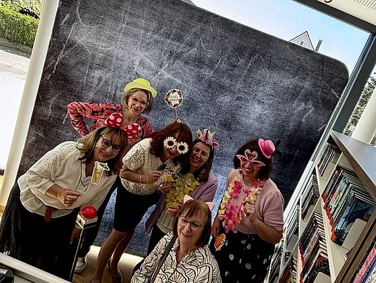 Eine Gruppe verkleideter Frauen posiert lachend vor einer Fotowand in der Bücherei.