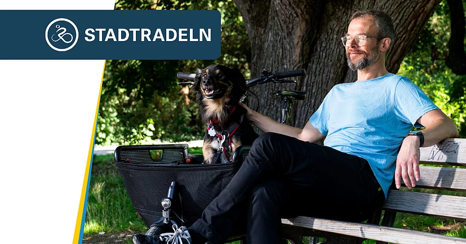 Ein Mann sitzt entspannt auf einer Parkbank im Schatten großer Bäume. Neben ihm befindet sich ein Fahrrad mit einem Korb, in dem ein kleiner schwarz-brauner Hund sitzt. Der Mann trägt ein hellblaues T-Shirt und blickt zufrieden zur Seite, während er den Hund streichelt. Oben links ist das Logo der Aktion „STADTRADELN“ eingeblendet.