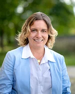 Eine Frau mit schulterlangen Haaren und hellem Blazer schaut offen und freundlich.