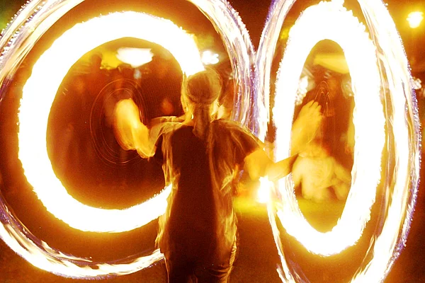 Ein Mensch mit zwei Feuerringen an den Armen während einer Feuershow.