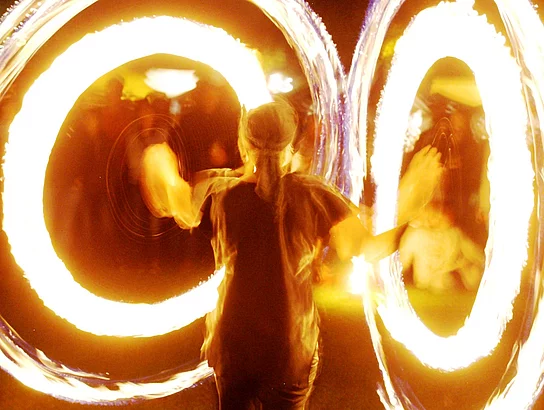 Ein Mensch mit zwei Feuerringen an den Armen während einer Feuershow.