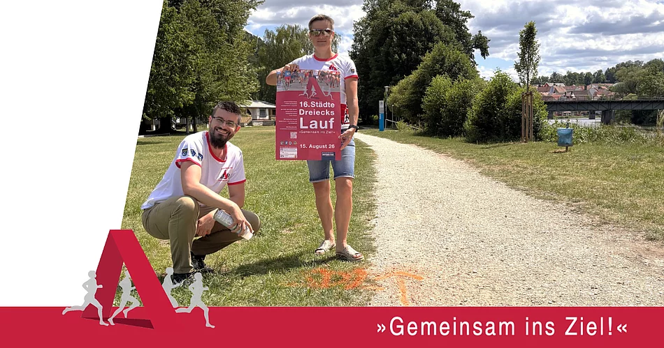Eine Werbegrafik zeigt zwei Personen in Laufshirts des Städtedreieckslaufs an einem geschotterten Uferweg. Eine Person kniet neben einer orangefarbenen Streckenmarkierung auf dem Boden, die andere hält das Veranstaltungsplakat des 16. Städtedreieckslaufs in die Kamera. Im Hintergrund sind Bäume, die Naab sowie eine Brücke zu sehen. Am unteren Bildrand steht der Slogan „Gemeinsam ins Ziel!“. Die Grafik weist darauf hin, dass die Laufstrecken bereits markiert sind und zum Training genutzt werden können.