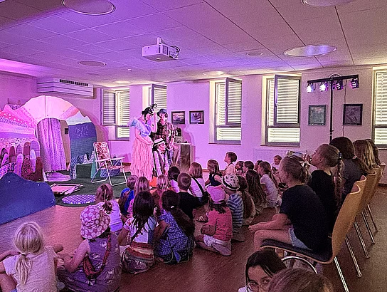 Kinder sitzen gespannt vor einer kleinen Theaterbühne und verfolgen die Aufführung des OVIGO Theaters.