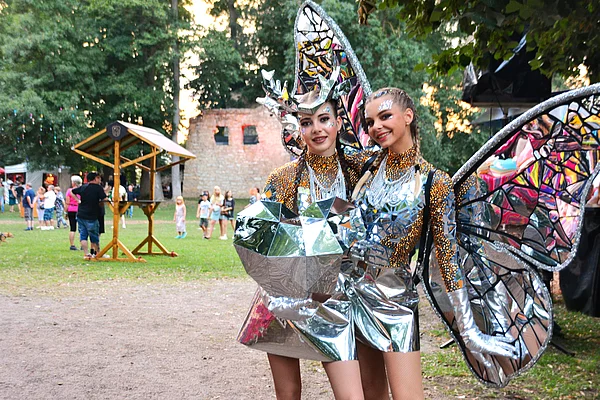 Zwei junge Frauen in einem verspiegelten Kostüm. Im Hintergrund die Schlossruine und Festbesucher.