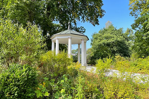 Ein weißer erbauter Pavillon mit prächtigen Säulen ragt aus Grünanlagen hervor.